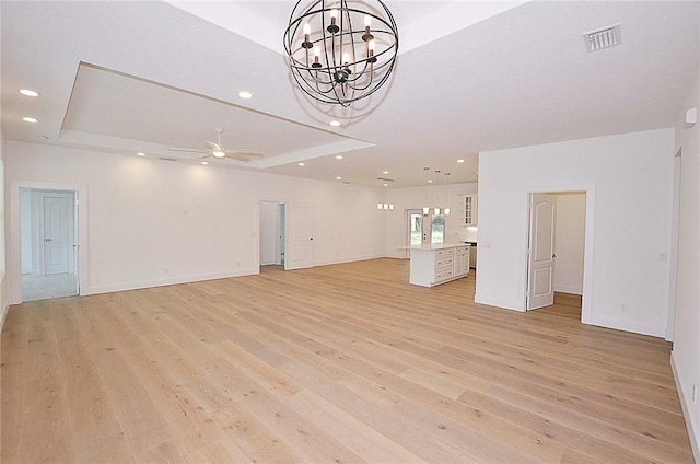 unfurnished living room featuring ceiling fan with notable chandelier, a raised ceiling, and light hardwood / wood-style flooring