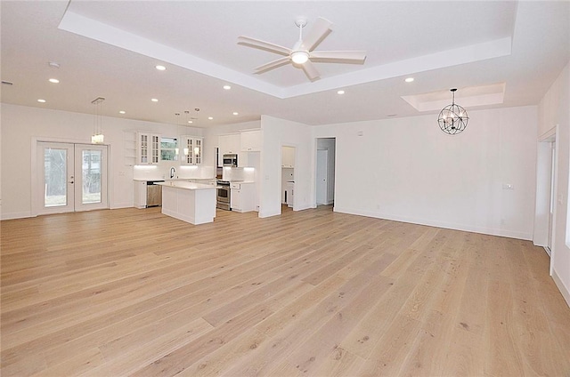 unfurnished living room featuring light hardwood / wood-style flooring, a raised ceiling, french doors, ceiling fan with notable chandelier, and sink