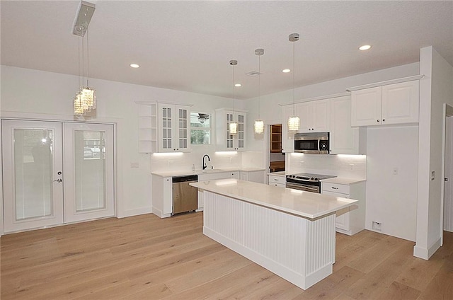 kitchen with appliances with stainless steel finishes, a center island, sink, white cabinetry, and decorative light fixtures