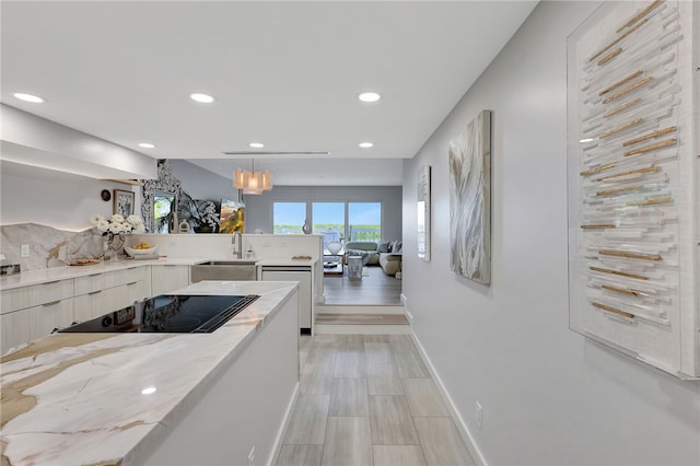 kitchen with black electric cooktop, sink, light stone counters, decorative light fixtures, and a chandelier