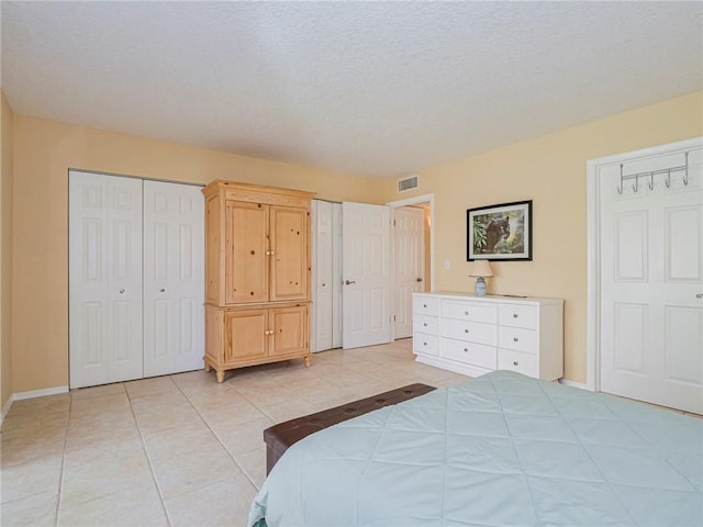 bedroom featuring baseboards, a textured ceiling, light tile patterned flooring, visible vents, and multiple closets