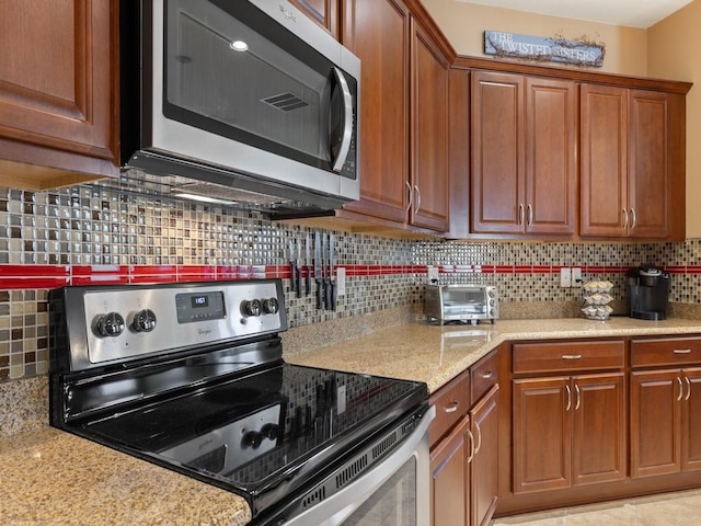 kitchen with tasteful backsplash, brown cabinets, light stone counters, and appliances with stainless steel finishes