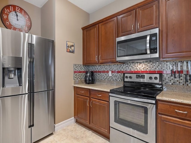 kitchen with brown cabinetry, appliances with stainless steel finishes, decorative backsplash, and light tile patterned floors