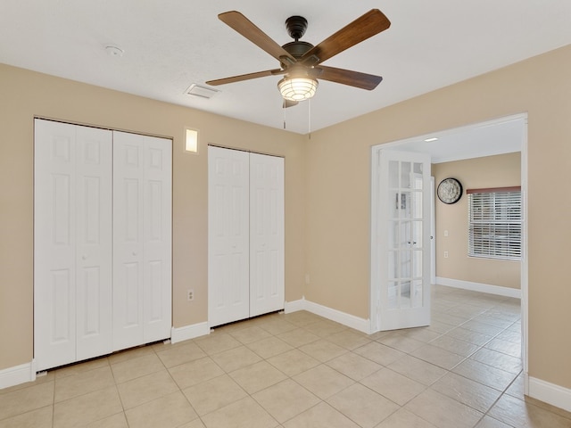 unfurnished bedroom featuring ceiling fan, light tile patterned floors, multiple closets, and french doors