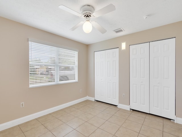 unfurnished bedroom featuring light tile patterned flooring, ceiling fan, a textured ceiling, and two closets