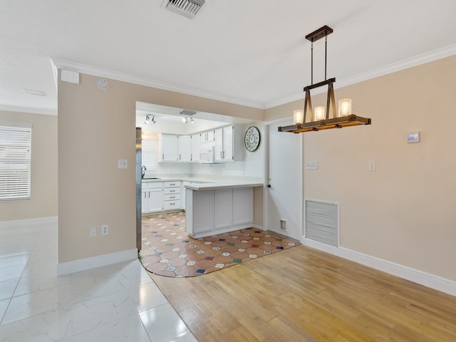 kitchen with ornamental molding, light wood-type flooring, hanging light fixtures, sink, and white cabinets