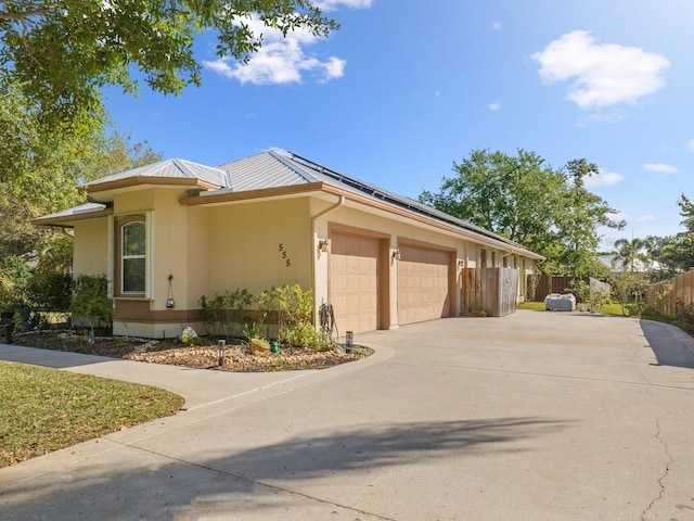 view of front of property featuring fence, driveway, solar panels, an attached garage, and stucco siding