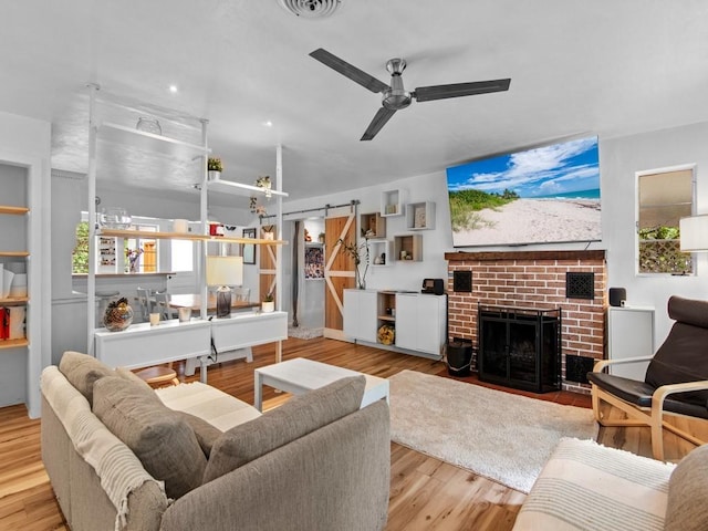 living area with a barn door, a fireplace, wood finished floors, visible vents, and a ceiling fan