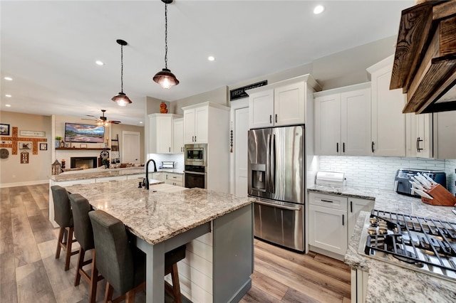 kitchen featuring stainless steel appliances, light wood-type flooring, an island with sink, white cabinets, and a breakfast bar area