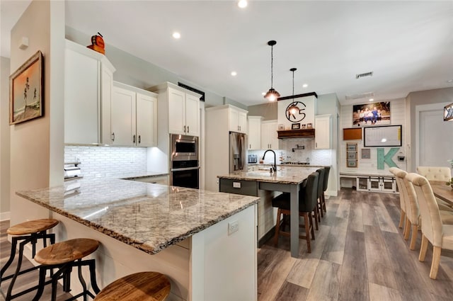 kitchen with stainless steel appliances, dark wood-type flooring, white cabinets, hanging light fixtures, and backsplash