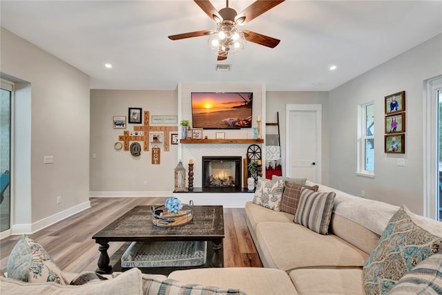 living room with a fireplace, ceiling fan, and light wood-type flooring