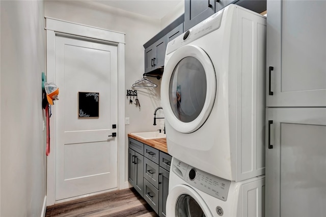 washroom with stacked washer and dryer, wood-type flooring, cabinets, and sink