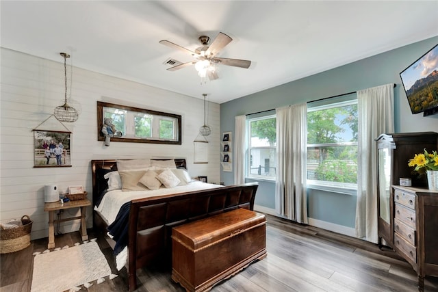 bedroom featuring hardwood / wood-style floors, wood walls, and ceiling fan