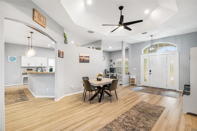 dining space featuring ceiling fan, a tray ceiling, sink, and light wood-type flooring