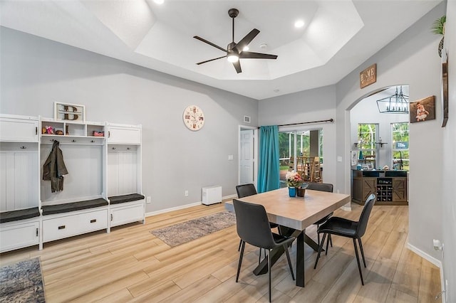 dining room featuring ceiling fan with notable chandelier, a tray ceiling, and light hardwood / wood-style floors