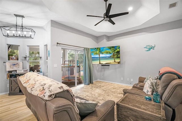 living room with ceiling fan with notable chandelier, a tray ceiling, and light hardwood / wood-style floors