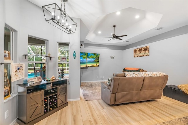 living room featuring ceiling fan, a tray ceiling, and light wood-type flooring