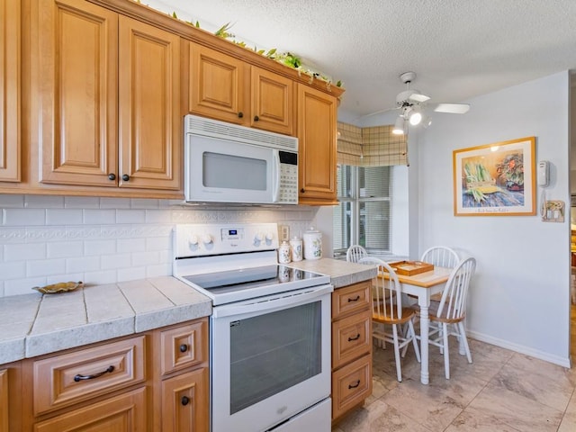 kitchen featuring ceiling fan, backsplash, tile countertops, a textured ceiling, and white appliances