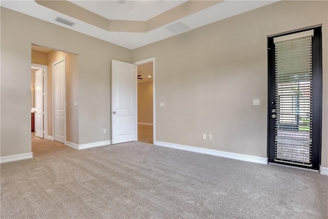 spare room featuring ceiling fan, light colored carpet, and a raised ceiling