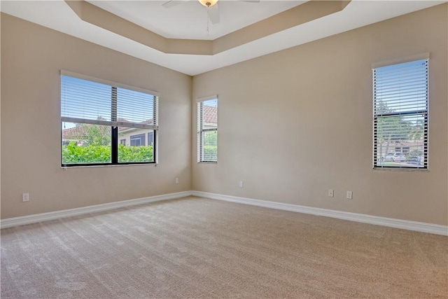 carpeted spare room featuring ceiling fan and a raised ceiling