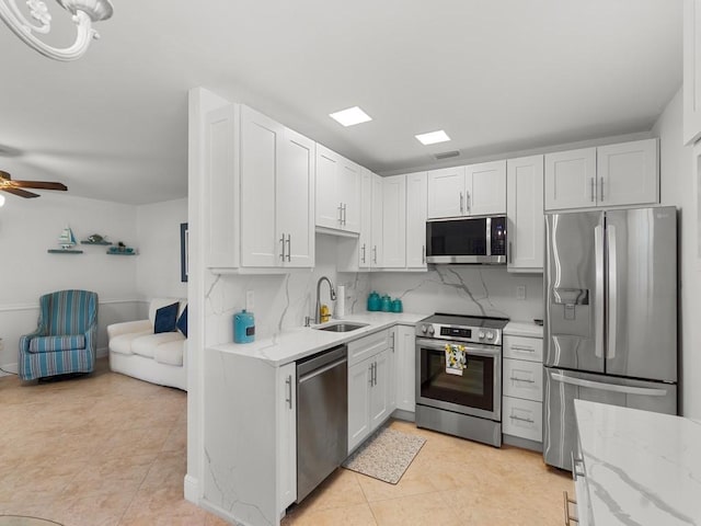 kitchen with light stone countertops, open floor plan, ceiling fan, a sink, and appliances with stainless steel finishes