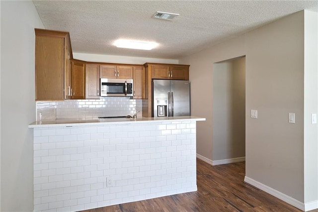 kitchen with visible vents, stainless steel appliances, a peninsula, brown cabinetry, and dark wood-style flooring