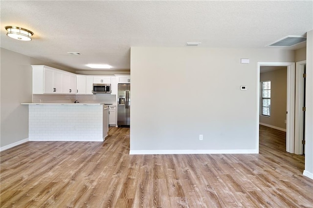 kitchen with stainless steel appliances, a peninsula, light wood-style flooring, and light countertops