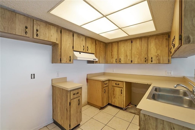 kitchen featuring under cabinet range hood, light countertops, brown cabinets, light tile patterned flooring, and a sink