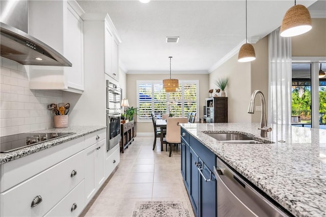 kitchen featuring white cabinets, wall chimney range hood, sink, blue cabinetry, and appliances with stainless steel finishes