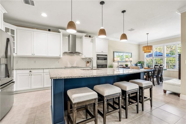 kitchen with hanging light fixtures, wall chimney range hood, crown molding, a center island with sink, and appliances with stainless steel finishes