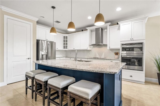 kitchen with stainless steel appliances, a center island with sink, hanging light fixtures, and wall chimney exhaust hood