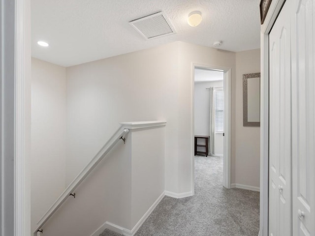 corridor featuring a textured ceiling and light colored carpet