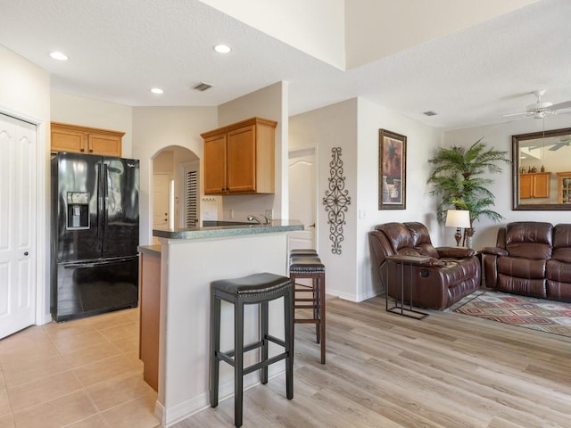 kitchen with black refrigerator with ice dispenser, kitchen peninsula, light hardwood / wood-style floors, a textured ceiling, and a breakfast bar