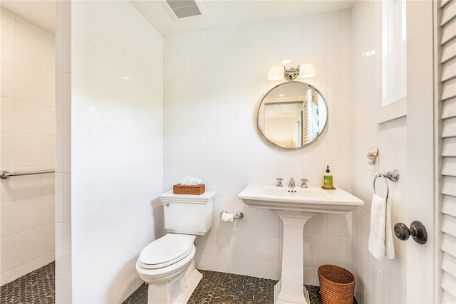 bathroom featuring tile walls, toilet, visible vents, and a sink