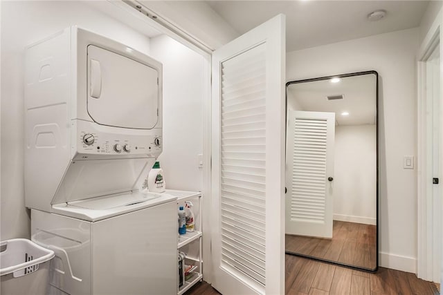 laundry area featuring wood finished floors, baseboards, visible vents, laundry area, and stacked washer / drying machine