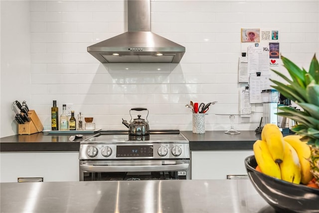 kitchen featuring dark countertops, tasteful backsplash, white cabinetry, stainless steel range with electric cooktop, and wall chimney exhaust hood