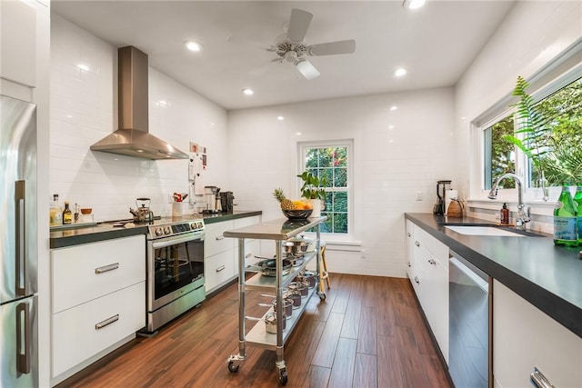 kitchen with dark countertops, stainless steel appliances, wall chimney exhaust hood, and a sink