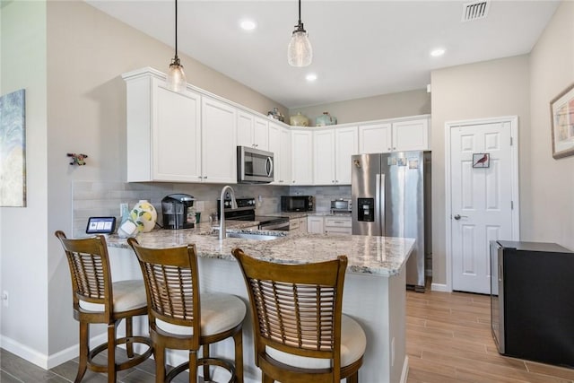 kitchen with light stone counters, a peninsula, visible vents, appliances with stainless steel finishes, and backsplash