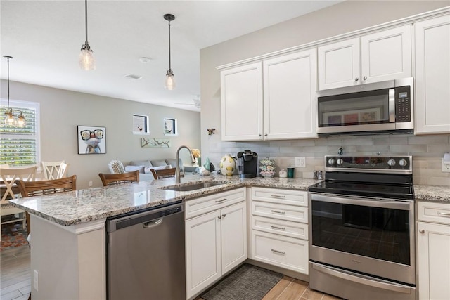 kitchen featuring stainless steel appliances, a peninsula, a sink, backsplash, and light wood finished floors