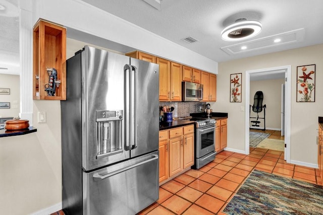 kitchen with light tile patterned floors, stainless steel appliances, dark countertops, visible vents, and decorative backsplash