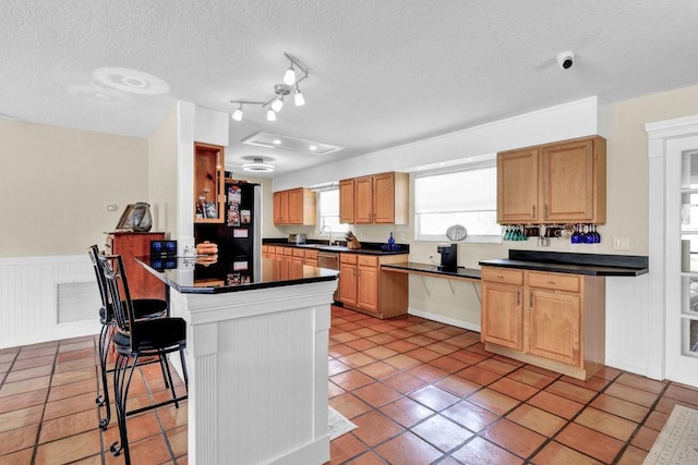 kitchen with a textured ceiling, a peninsula, a breakfast bar, wainscoting, and dark countertops