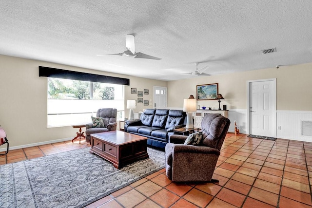 living room featuring visible vents, a ceiling fan, wainscoting, a textured ceiling, and tile patterned floors