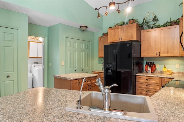 kitchen featuring sink, light stone countertops, a kitchen island, black fridge with ice dispenser, and washer / clothes dryer