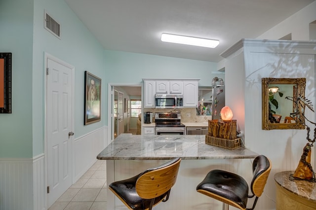 kitchen featuring white cabinets, a kitchen bar, stainless steel appliances, and kitchen peninsula