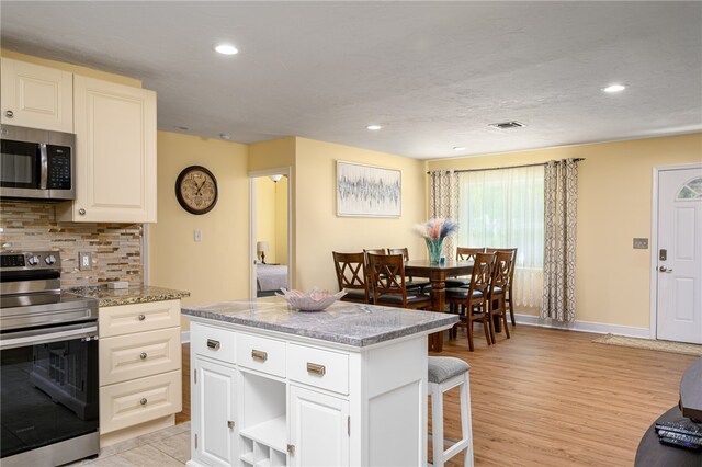 kitchen featuring appliances with stainless steel finishes, light stone countertops, light hardwood / wood-style flooring, a center island, and decorative backsplash