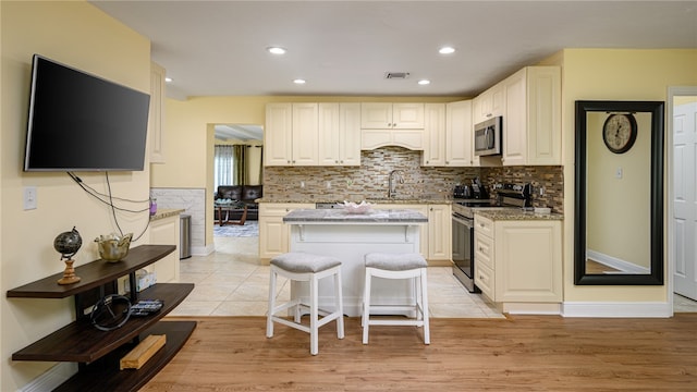 kitchen with stainless steel appliances, a kitchen bar, light stone countertops, sink, and light hardwood / wood-style floors