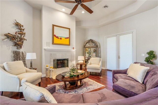 living room with a tiled fireplace, dark hardwood / wood-style flooring, and ceiling fan