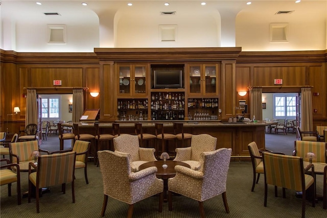 bar with plenty of natural light, wooden walls, a high ceiling, and dark colored carpet