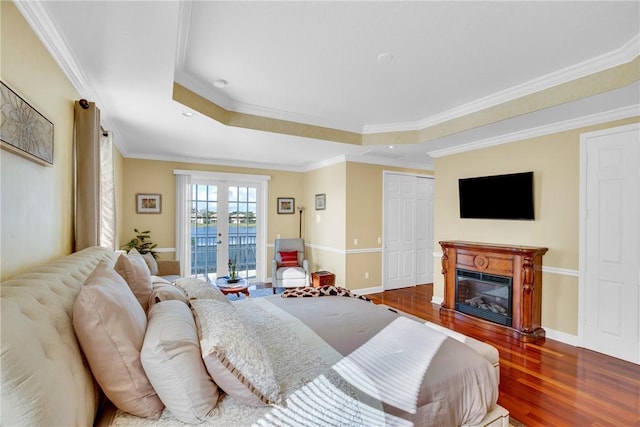 bedroom with a tray ceiling, crown molding, dark hardwood / wood-style flooring, and french doors