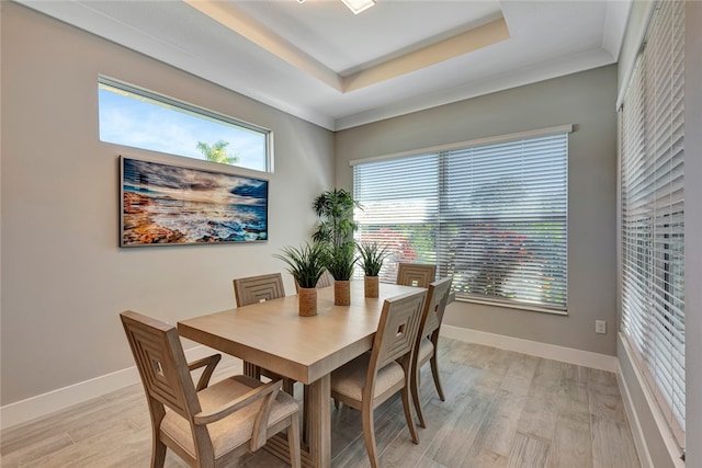 dining room with ornamental molding, a tray ceiling, light hardwood / wood-style flooring, and a healthy amount of sunlight